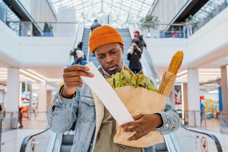 Surprised black man looks at receipt total with food in mall