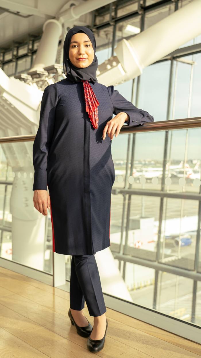 A woman models a long navy jacket over trousers, with a hijab